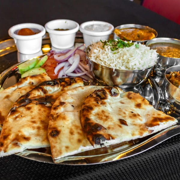 A silver platter of Indian food with naan bread, rice, curries, and condiments.