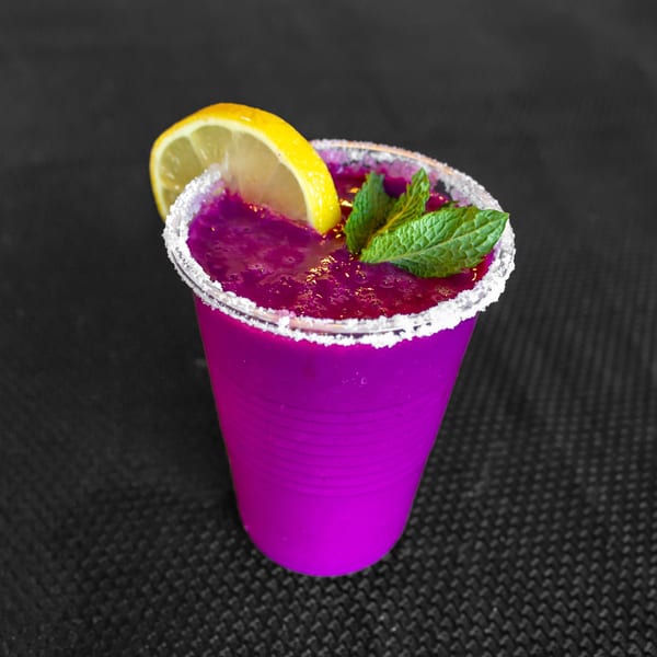 Vibrant purple drink in a clear cup with a sugar rim, garnished with lemon and mint.
