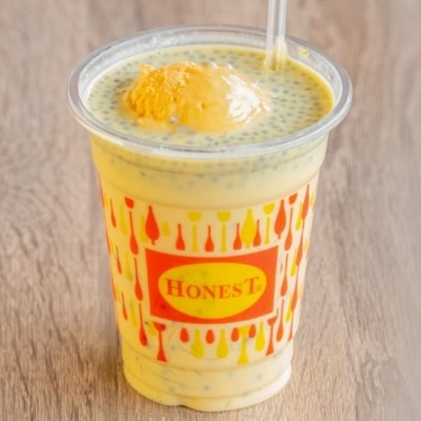 A yellow mango lassi drink with a scoop of ice cream and chia seeds in a branded Honest cup.