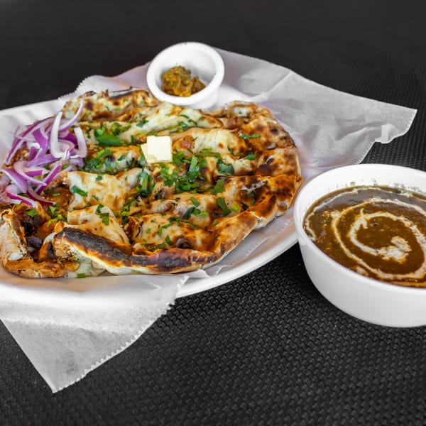 Indian naan bread with red onions, cilantro, and butter, served with a side of dal makhani.