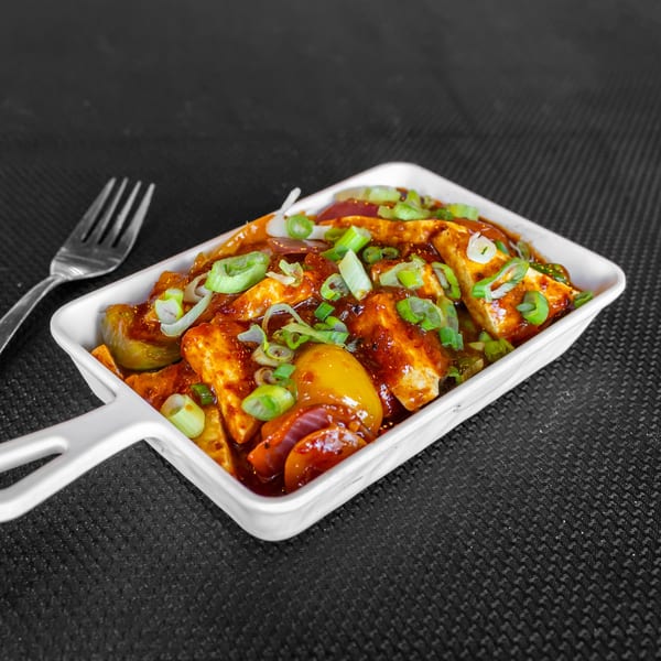 Chilli Paneer, an Indian dish with paneer, bell peppers, and onions in a rich sauce, garnished with scallions.