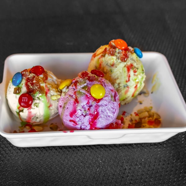 Three scoops of Indian ice cream, topped with colorful candies and fruit, in a white dish.